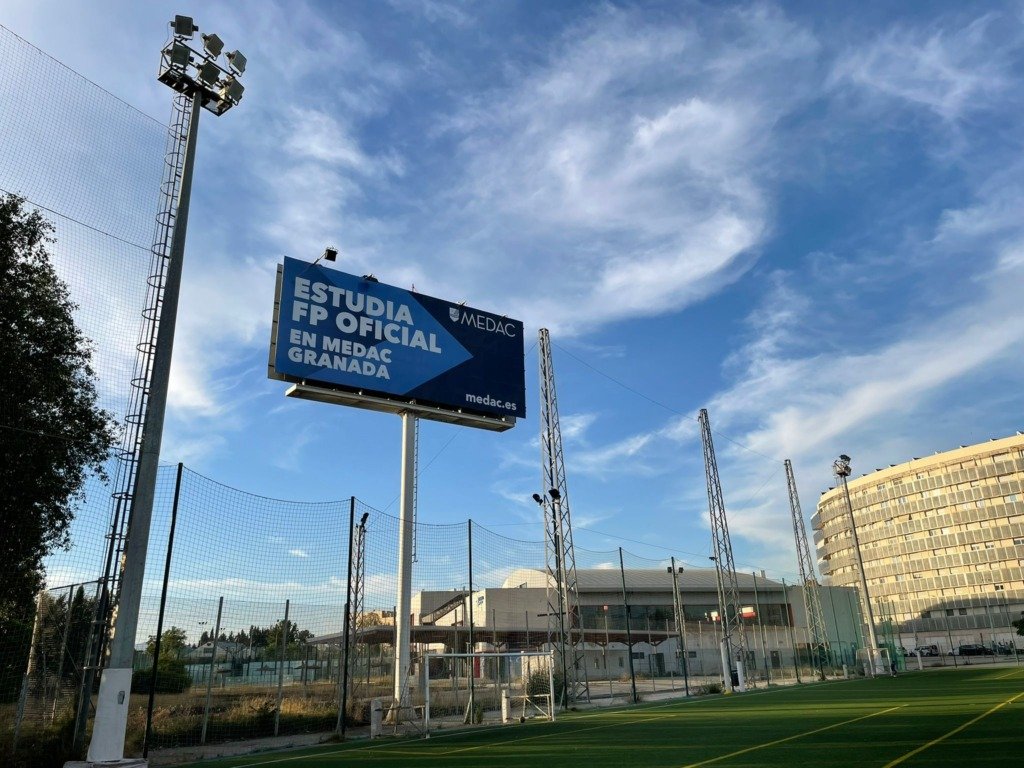 Poste publicitario de gran altura con valla de MEDAC junto a unas instalaciones deportivas en Granada